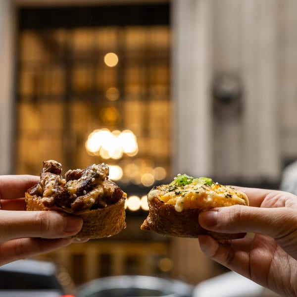 Two hands holding different Yum Yubu poke bites, with a blurred restaurant background.