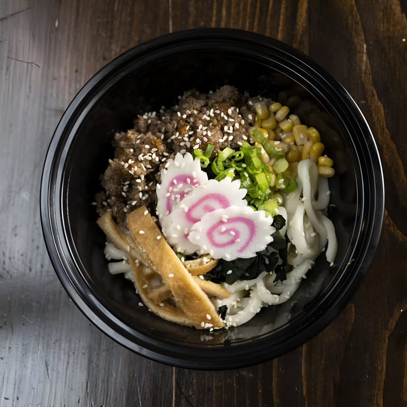 Yum Yubu poke bowl with ground meat, corn, green onions, fish cakes, and noodles.