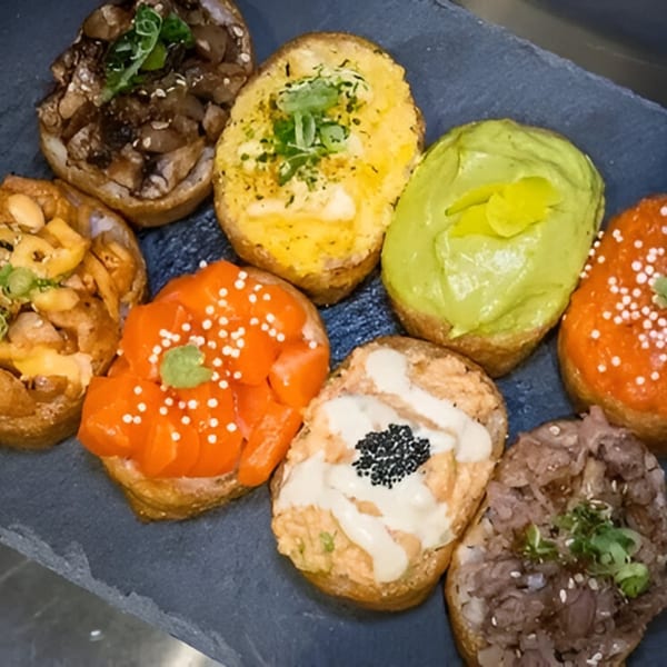 Assortment of colorful Yum Yubu poke bites with various toppings on a dark slate board.